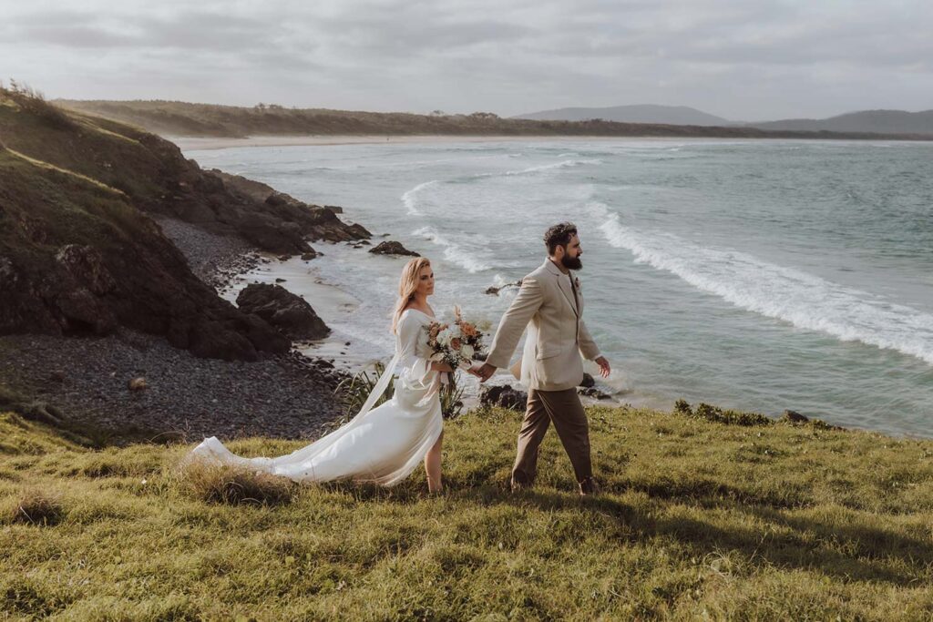 Bride and groom walking on a headland with the ocean behind them