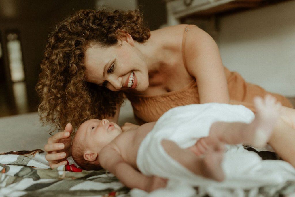 newborn is laying on the floor and her mum is looking down at her smiling at  a in home newborn phot session