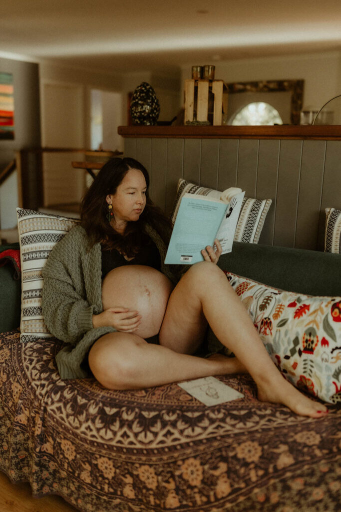 pregnant woman relaxing and reading a book on the couch at a maternity photo shoot at Coffs Harbour