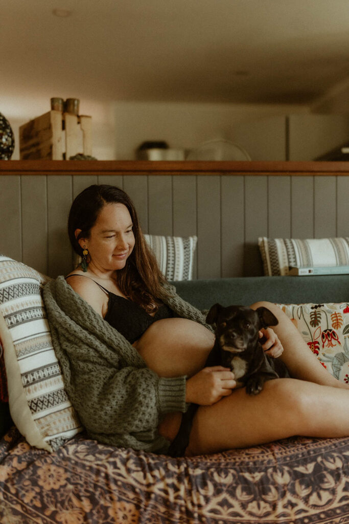 Pregnant woman on the couch cuddling her dog and smiling.