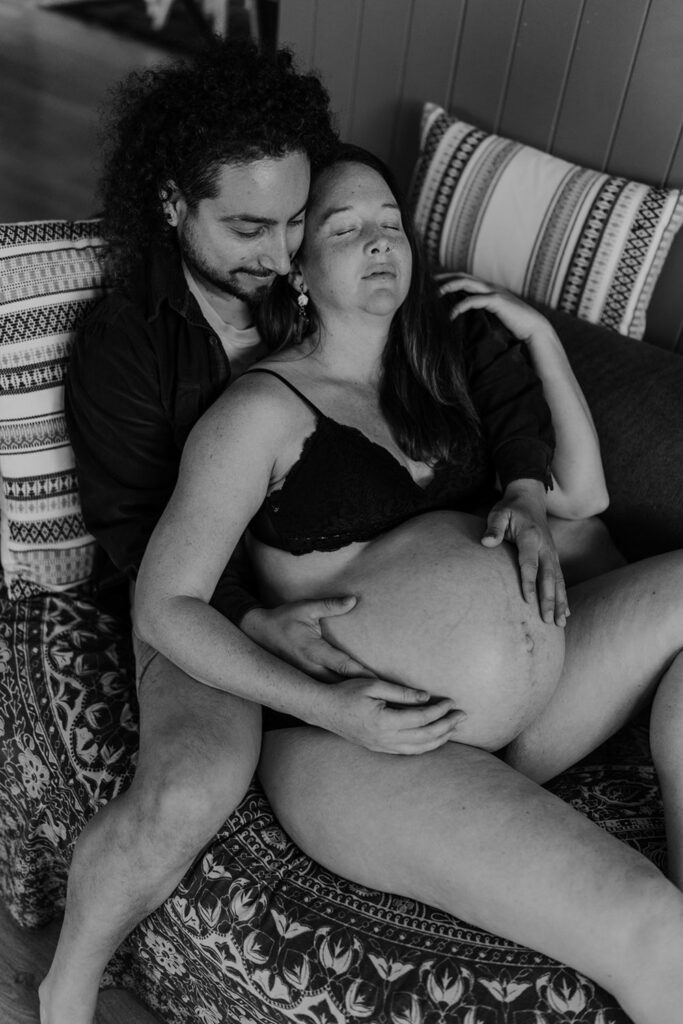 Pregnant couple relaxing on the couch eyes closed and snuggling a maternity photo session.